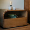 A small wooden nightstand with a lamp on top in a cozy bedroom setting.